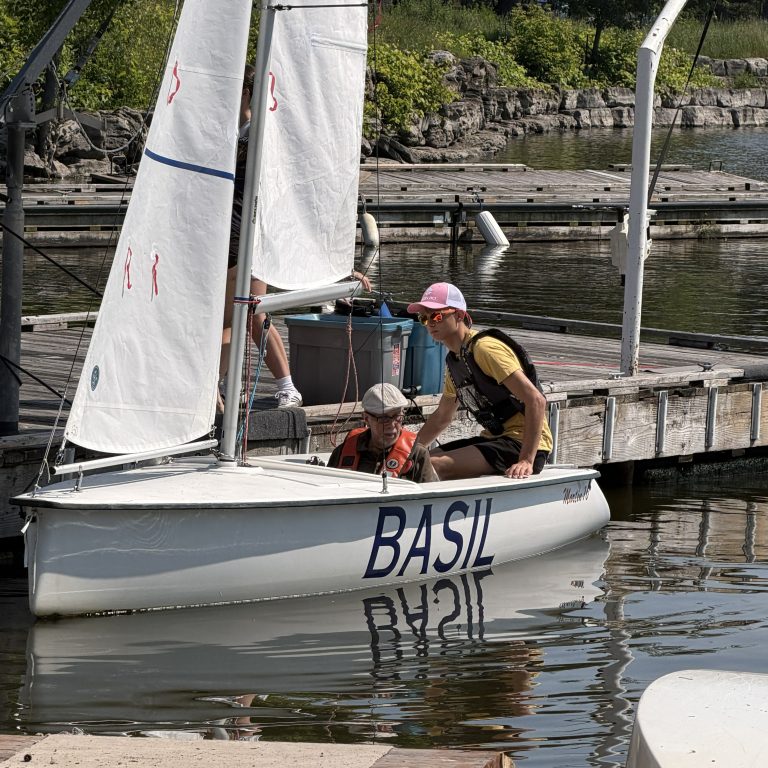 Bateau à voile "BASIL" avec deux hommes, prêt pour une sortie sur l'eau.