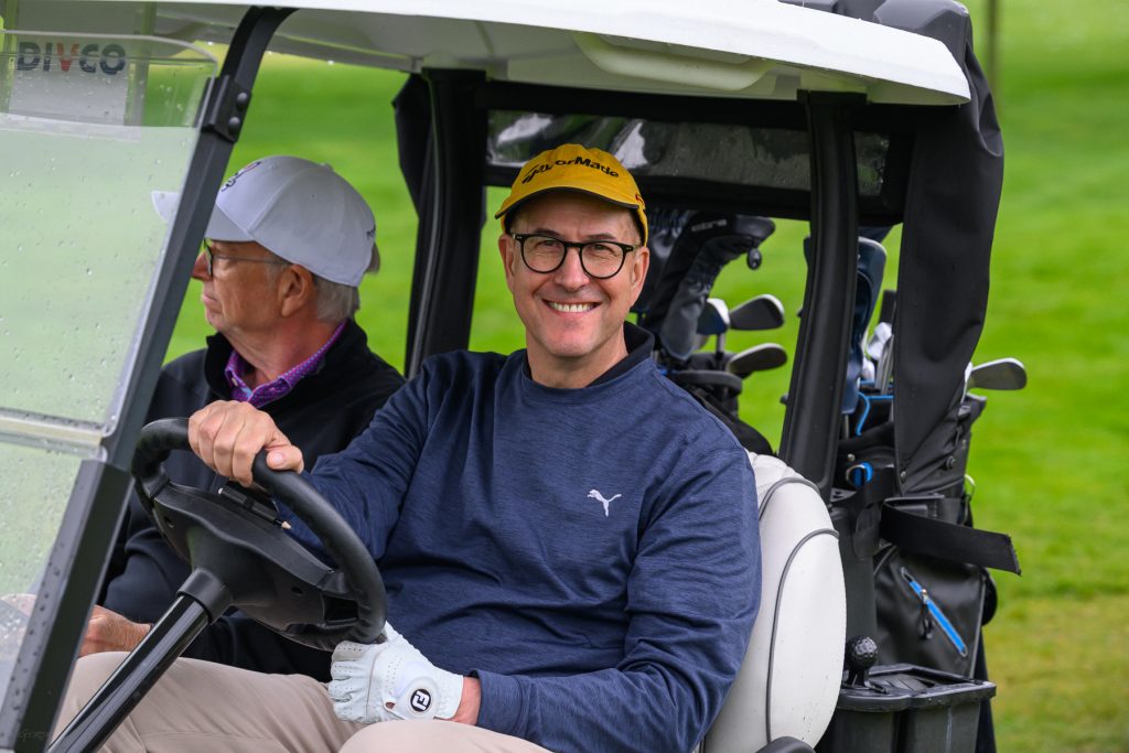 Deux golfeurs souriants dans un chariot de golf, sur un parcours de golf.