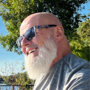 Jean-Pierre Morier souriant, portant des lunettes de soleil, à l'extérieur.